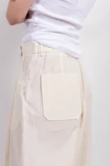 Pantalón de vestir color crema, de tiro medio y corte ancho. Presenta pinzas en la parte delantera y largo hasta los tobillos.