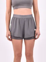 Short deportivo negro de doble capa, con una capa exterior suelta y una capa interior ajustada tipo calza. Presenta un detalle vertical blanco en el lateral derecho.