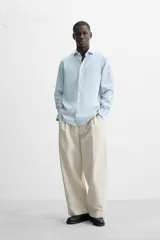Camisa celeste a rayas verticales, de corte regular fit, con cuello italiano abierto, mangas largas con puños abotonados y cierre frontal con botones.