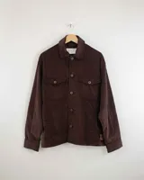 Camisa de pana color beige, de manga larga, con cuello camisero, cierre frontal de botones y dos bolsillos de parche con solapa en el pecho. Presenta un corte recto y holgado.