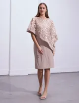 Vestido de fiesta color beige, de corte recto y largo a la rodilla, confeccionado en seda fría. Presenta una sobrecapa de microtul bordado con motivos florales.