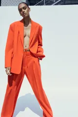 Pantalón de vestir color naranja, de tiro alto y pernera ancha. Presenta doble pliegue frontal, trabillas en la cintura, bolsillos laterales y falsos bolsillos de vivo en la espalda.