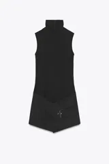 Mono corto negro con cuello alto y sin mangas. La parte inferior simula una falda cruzada con cinturón y hebilla metálica. Cierre trasero con cremallera oculta.