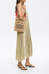 Bolso tote de rafia color beige con diseño calado, asas cortas de cuero marrón y cordones rojos decorativos.