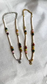 Gargantilla corta de cuentas pequeñas color blanco, con cuentas grandes de colores (rosa, verde, marrón y amarillo) y dije de cristal transparente.