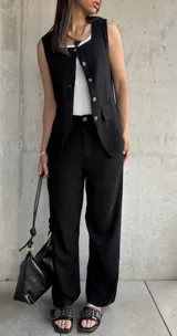 Conjunto negro de chaleco con botones y pantalón de vestir de corte recto. El chaleco tiene cuello cuadrado con ribete blanco y bolsillos delanteros. El pantalón es de tiro alto y pierna ancha.