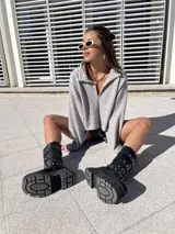 Bota negra de ecocuero con caña media, plataforma track y tres correas con hebillas plateadas.