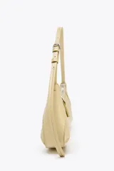 Bolso de hombro color crema con forma alargada, asa ajustable con hebilla, bolsillo interior con cremallera y cierre con cremallera y tirador.