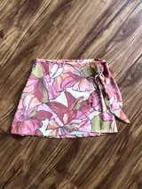 Minifalda pareo con estampado floral en tonos rosa, naranja, verde y blanco. Se ata a la cintura con un lazo lateral.