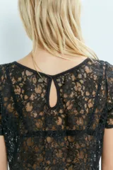 Remera de encaje negro con lentejuelas, cuello bote y mangas cortas.