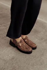 Zuecos de cuero con estampado snake, hebilla lateral metálica, puntera cuadrada y base robusta.