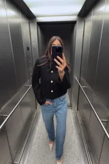 Cazadora corta negra de cuello redondo y manga larga. Tiene bolsillos delanteros de plastrón y cierre frontal con botones dorados.