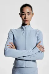 Campera deportiva corta celeste con cuello alto, cierre frontal, mangas largas con orificios para los pulgares y tecnología SoftMove™ y DryMove™.