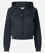 Campera rompevientos deportiva color blanco, confeccionada en poliamida, con capucha, cierre delantero en cremallera, tirador gomoso y puños ajustados.