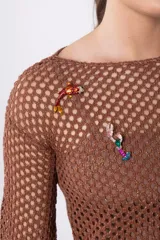 Top de tejido calado color marrón con mangas largas acampanadas y detalle de broches decorativos en el escote.