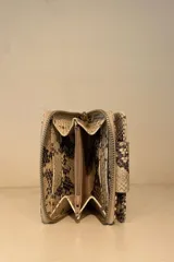 Billetera pequeña con estampado de piel de cocodrilo en tonos beige y marrón. Cierre con broche a presión y correa de muñeca.