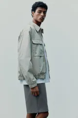 Campera color beige de corte holgado, con cuello camisero, cierre frontal y bolsillos superiores con solapa.