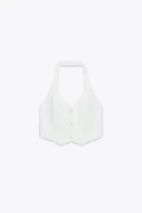 Chaleco blanco con cuello halter ajustable, escote pico, falsos bolsillos de vivo en delantero, detalle de costuras marcadas, forro interior a tono y cierre frontal con botones.