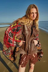 Poncho de cuero ovino con corte de chaqueta y mangas tejidas en lana con diseño geométrico multicolor. Talle único.