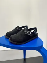 Zuecos negros con capellada de pelo sintético, tira trasera con hebilla metálica y suela track.