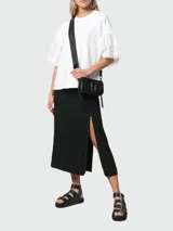 Bolso cruzado Marc Jacobs modelo The Snapshot DTM, color negro brillante, con correa ancha negra estampada con el logo de la marca. Presenta herrajes metálicos plateados y el logo de doble "J" en el frente.