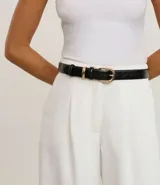 Cinturón femenino mediano de poliuretano negro con textura de cocodrilo (crocco). Posee una hebilla redondeada y trabillas metálicas de color dorado.