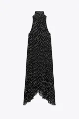 Vestido midi negro con estampado de lunares blancos, cuello halter con pañuelo integrado, sin mangas y bajo asimétrico. Cierre con abertura y botón en la nuca.