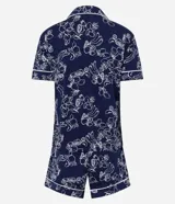 Pijama de dos piezas compuesto por una blusa de manga corta con cuello y cierre de botones, y un short con cintura elástica. El conjunto es de color azul marino con un estampado integral de flores y frutas en blanco, con ribetes blancos en los bordes.