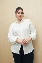 Camisa blanca de manga larga con textura sutil y caída fluida. Presenta cuello clásico, botones forrados a tono y puños con terminación fruncida.