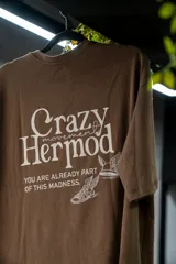 Remera oversize marrón de algodón elastizado con estampado en la espalda que incluye el texto "Crazy Hermod movement" y un diseño de zapatilla alada.