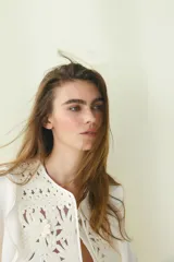 Blusa color crema de crepé de viscosa con mangas largas acampanadas y pechera con volados y bordado floral. Tiene cuello redondo y lazo para atar en el frente.