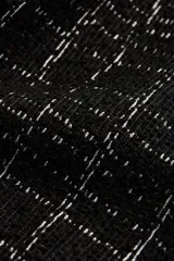 Top de bouclé negro con diseño a cuadros, cuello redondo y mangas cortas. Presenta botones decorativos en el hombro.