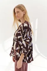 Camisa marrón con estampado de hojas blancas y azules, corte holgado, cuello mao, manga 3/4 y cierre frontal con botones.