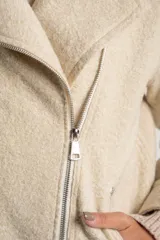 Campera de abrigo color crema, con cuello solapa y cierre frontal asimétrico. Presenta textura bouclé o de lana rizada.