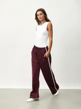 Pantalón deportivo color borgoña, de corte ancho y cintura elástica. Presenta una franja blanca vertical a lo largo de la pierna.