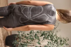 Chaleco marrón de cuero con cuello en V, cierre frontal con broches metálicos y detalle de tachas en el borde. Diseño con paneles y flecos en la parte inferior.