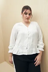 Camisa marrón de manga larga con escote en V y botones forrados al tono en el frente. Destaca por su textura sutil y por el detalle de frunces con volados en la parte inferior.