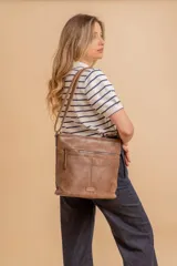 Cartera tipo bandolera de tamaño mediano confeccionada en símil cuero color marrón. Presenta una correa larga regulable, dos compartimientos principales y un bolsillo frontal con cierre de cremallera.