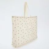 Bolso tipo tote bag grande de tela color beige con estampado de cerezas rojas y hojas verdes.