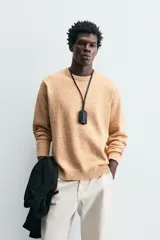 Sweater color arena con textura jaspeada, de corte recto, cuello redondo y mangas largas con terminaciones acanaladas.