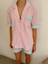Conjunto de pijama de algodón a rayas verticales rosas y blancas, con detalles en celeste. Incluye camisa de manga corta con botones y bolsillo en el pecho, y shorts con cintura elástica.