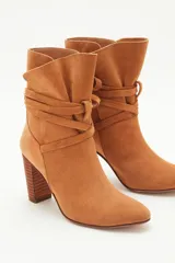 Botas de caña media de gamuza negra, con taco cuadrado y punta fina. Presenta tiras terminadas con borlas que se cruzan y atan alrededor de la caña.