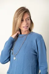 Sweater rojo de punto con cuello redondo y mangas largas. Presenta detalle de trenzado y distintos puntos en el frente, y dos bolsillos delanteros.