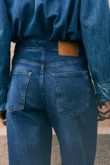 Pantalón de jean de tiro extra alto, color azul oscuro con efecto desgastado sutil. Corte de pierna amplia y recta, con puños anchos doblados. Presenta bolsillos parche cuadrados en la parte trasera y cierre expuesto en la espalda.