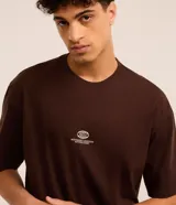 Remera marrón de corte relajado, cuello redondo y mangas cortas. Estampa frontal con un auto y la frase "Mindnight Legends Never Fade".