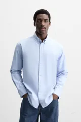 Camisa celeste de algodón, corte relaxed fit, cuello abotonado, manga larga con puños abotonados y cierre frontal con botones.