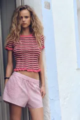 Camiseta de punto con rayas horizontales en tonos rosa, marrón y beige. Tiene cuello redondo con ribete y mangas cortas con volantes en los extremos.