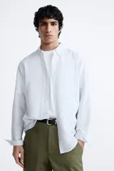Camisa celeste a rayas verticales, de corte relaxed fit, confeccionada en lino y algodón. Tiene cuello abotonado, manga larga con puños abotonados, bolsillo de parche en el pecho y cierre frontal con botones.