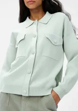 Chaqueta color verde agua con cuello camisero, cierre frontal con botones, dos bolsillos de parche con solapa en el pecho y mangas largas.