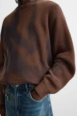 Sweater marrón de punto con cuello redondo y manga larga. Tiene un estampado irregular con efecto spray en color azul.